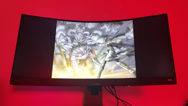 scene from an anime on a curved monitor against a red wall