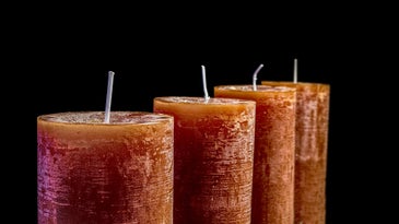 four orange candles are in a row with a black background