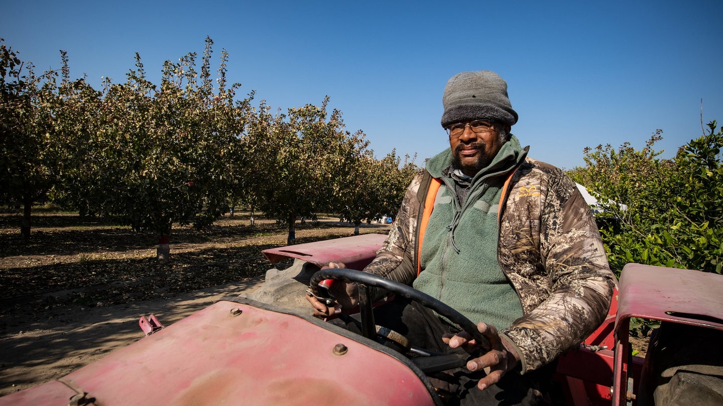Black farmer on a no-till tractor with pistachio trees in the background