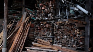 A lot of logs, rough-sawn wood, and assorted planks stacked up in a barn of some kind.