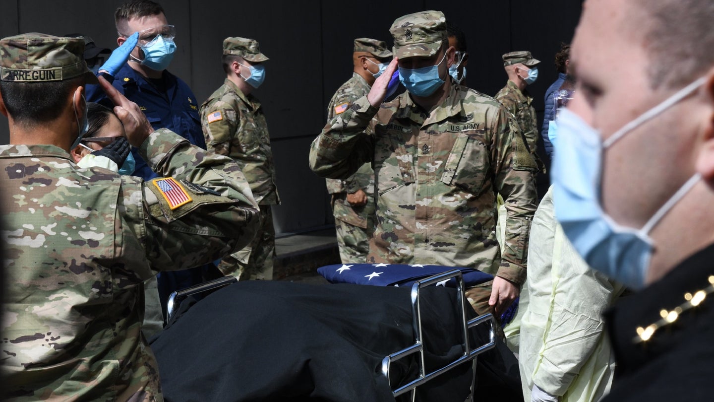 US Army service members in surgical masks saluting the coffin of a veteran who died of COVID-19