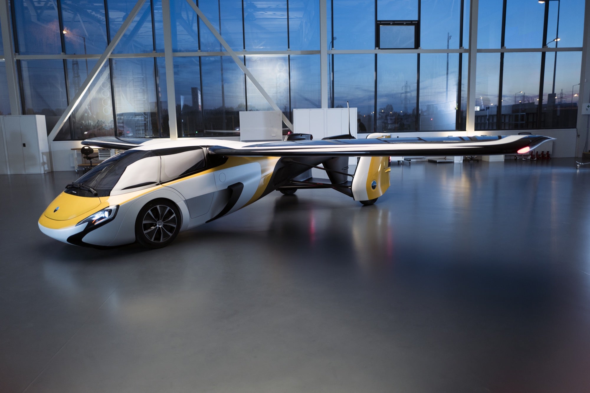 a modern hybrid car airplane model in yellow and white in an indoor hanger