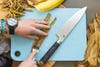 A person shredding banana peels with a fork on a teal plastic cutting board, with a knife on the cutting board and banana peels all around it.