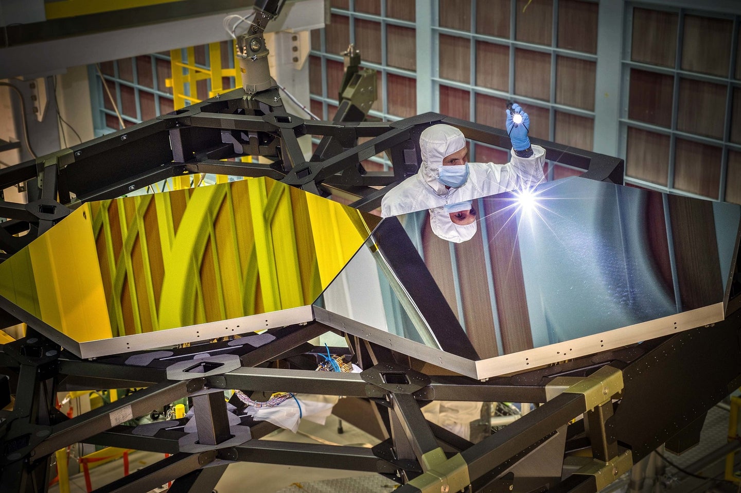 NASA James Webb Space Telescope's primary mirror segments, shaped as hexagons and coated in gold, being inspected by an engineer prior to launch