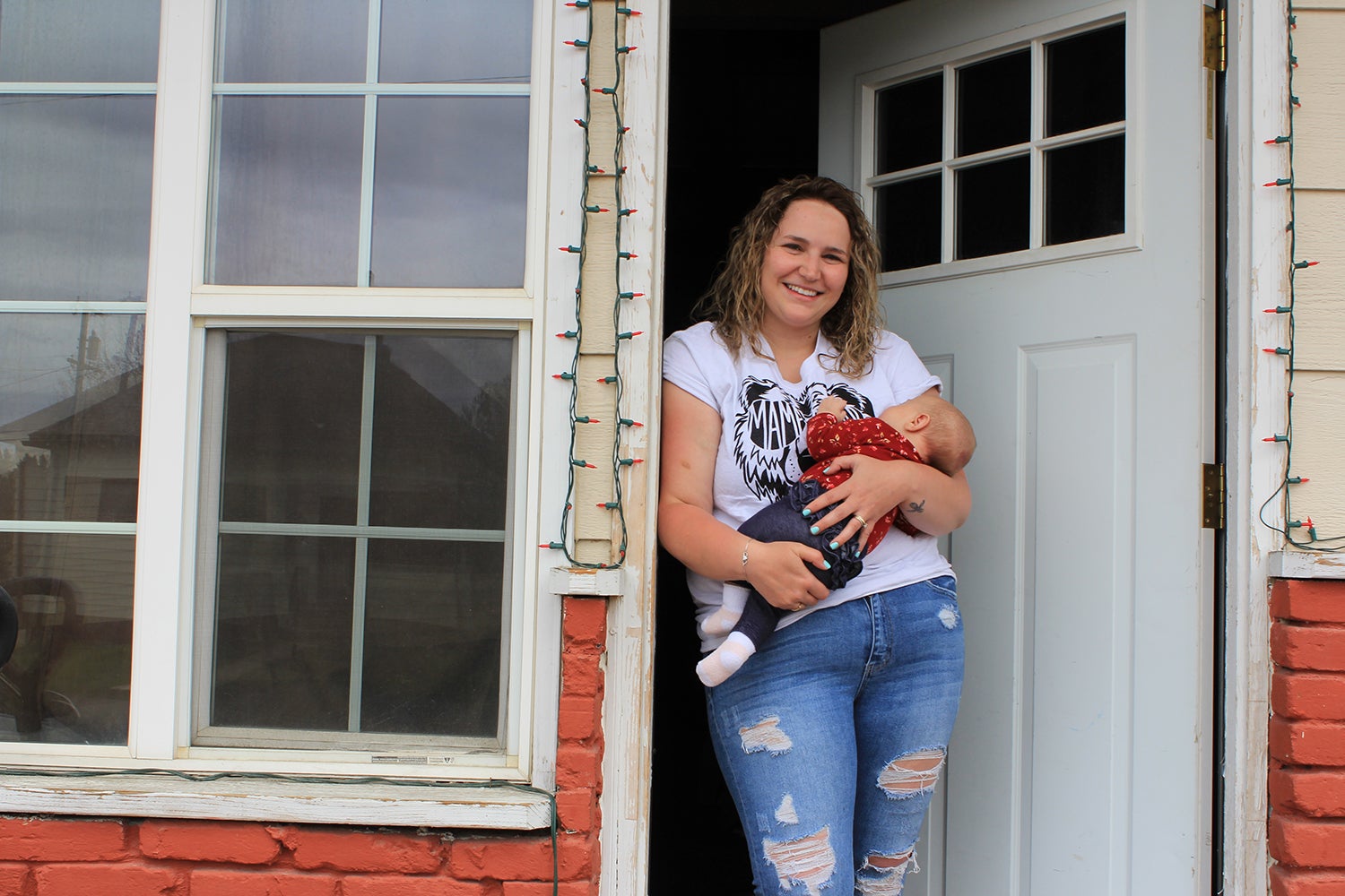 Haley Rehm holds her 2-month-old baby in the doorway of her home just across the street from the Continental mine in Butte, Montana. Rehm didn’t think about the dust often until a recent test of her 2-year-old son’s blood found elevated lead levels. (Katheryn Houghton/KHN)