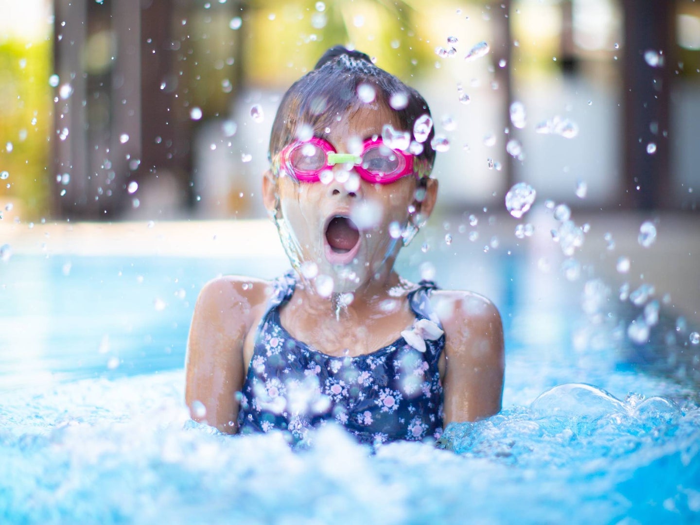 child jumping in pool with swimming goggles on