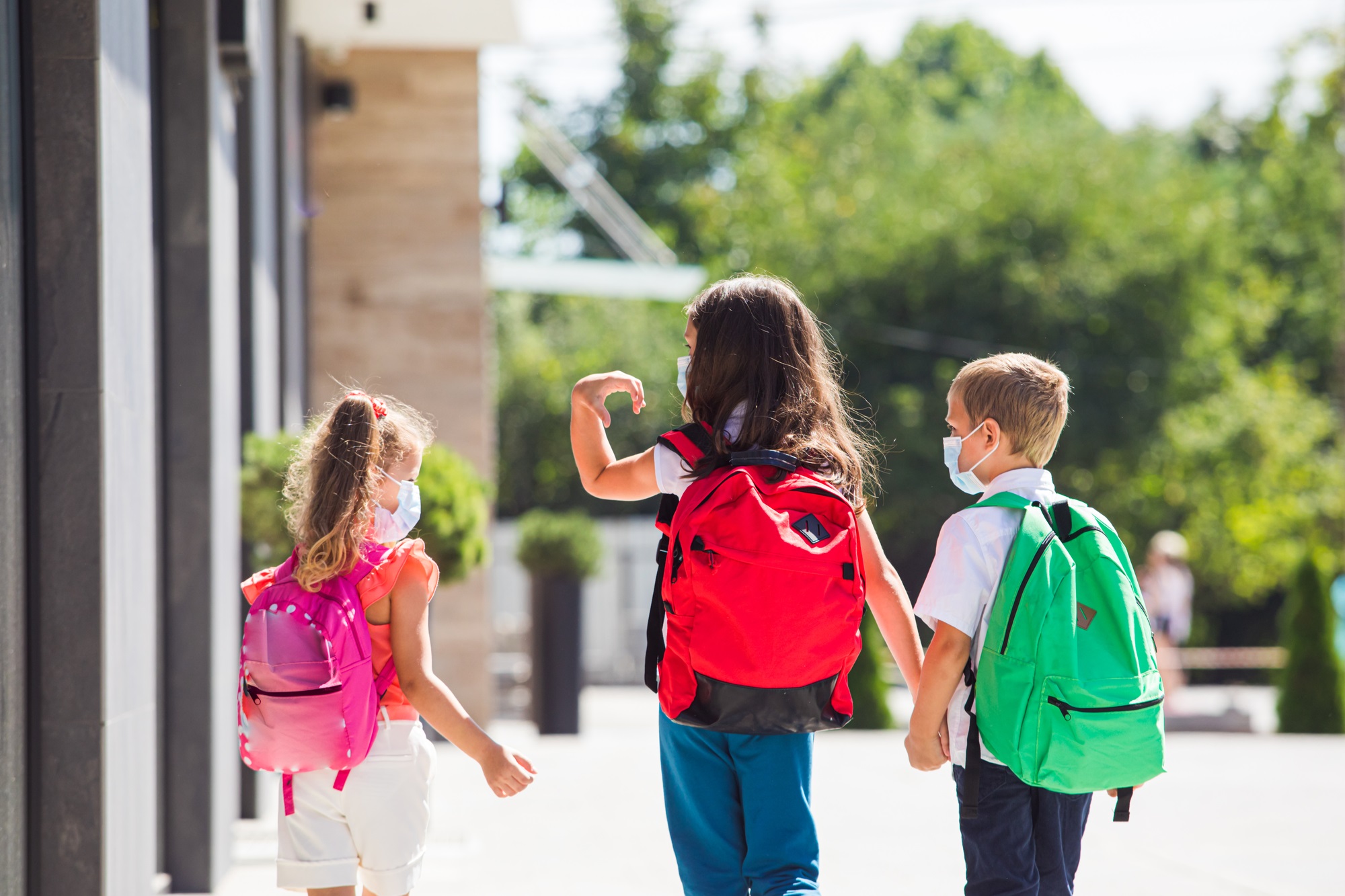 Three kids in COVID masks with bookbags right before summer vacation and COVID vaccines are available for their age group