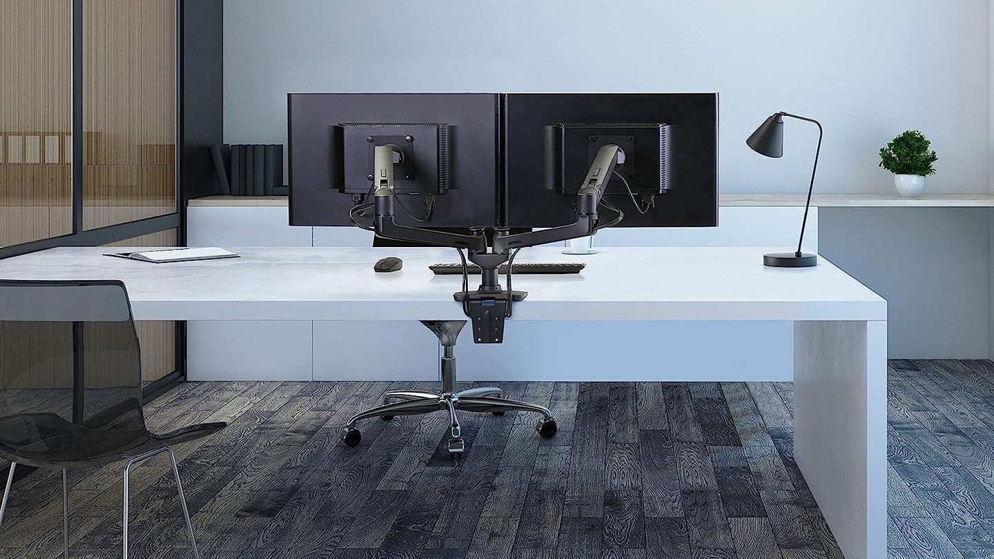 An Ergotron dual-monitor stand attached to a desk in a high-end office.