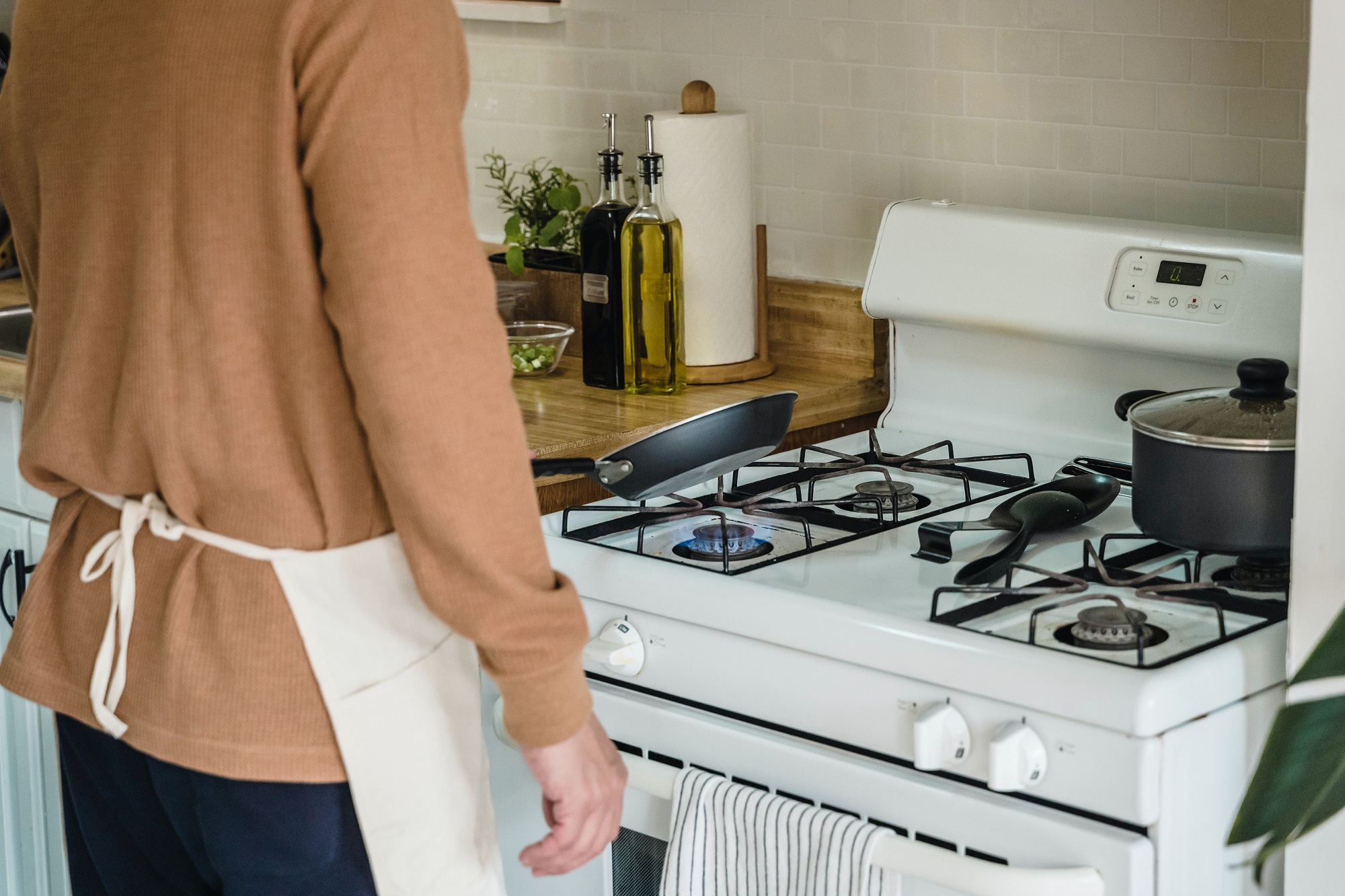 Person in brown sweater with a white apron frying something on a gas stove that's leaking methane