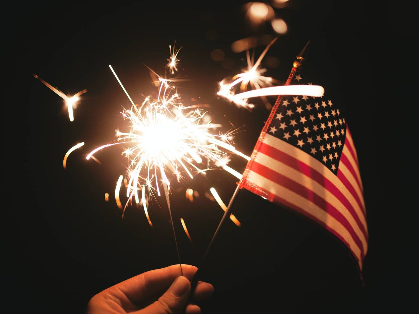 Hand holding firework and american flag against dark night