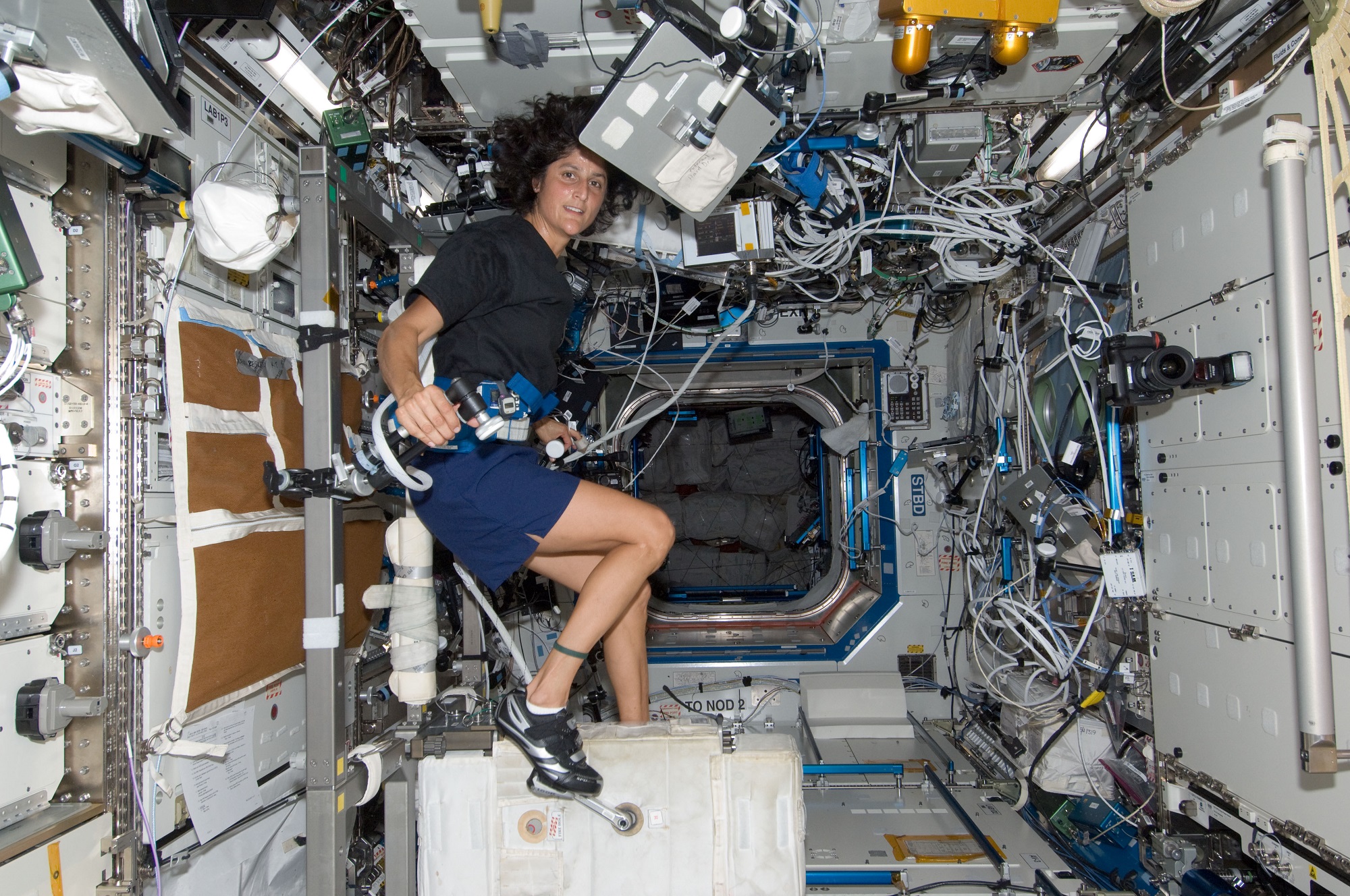 NASA astronaut with long brown hair and brown skin exercising on an erg machine in space to improve bone density