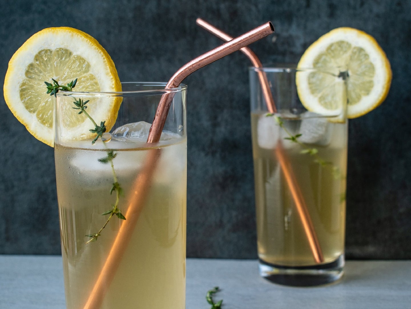 Yellow citrus home-brewed iced tea with lemon slices and metal straws in front of a black background