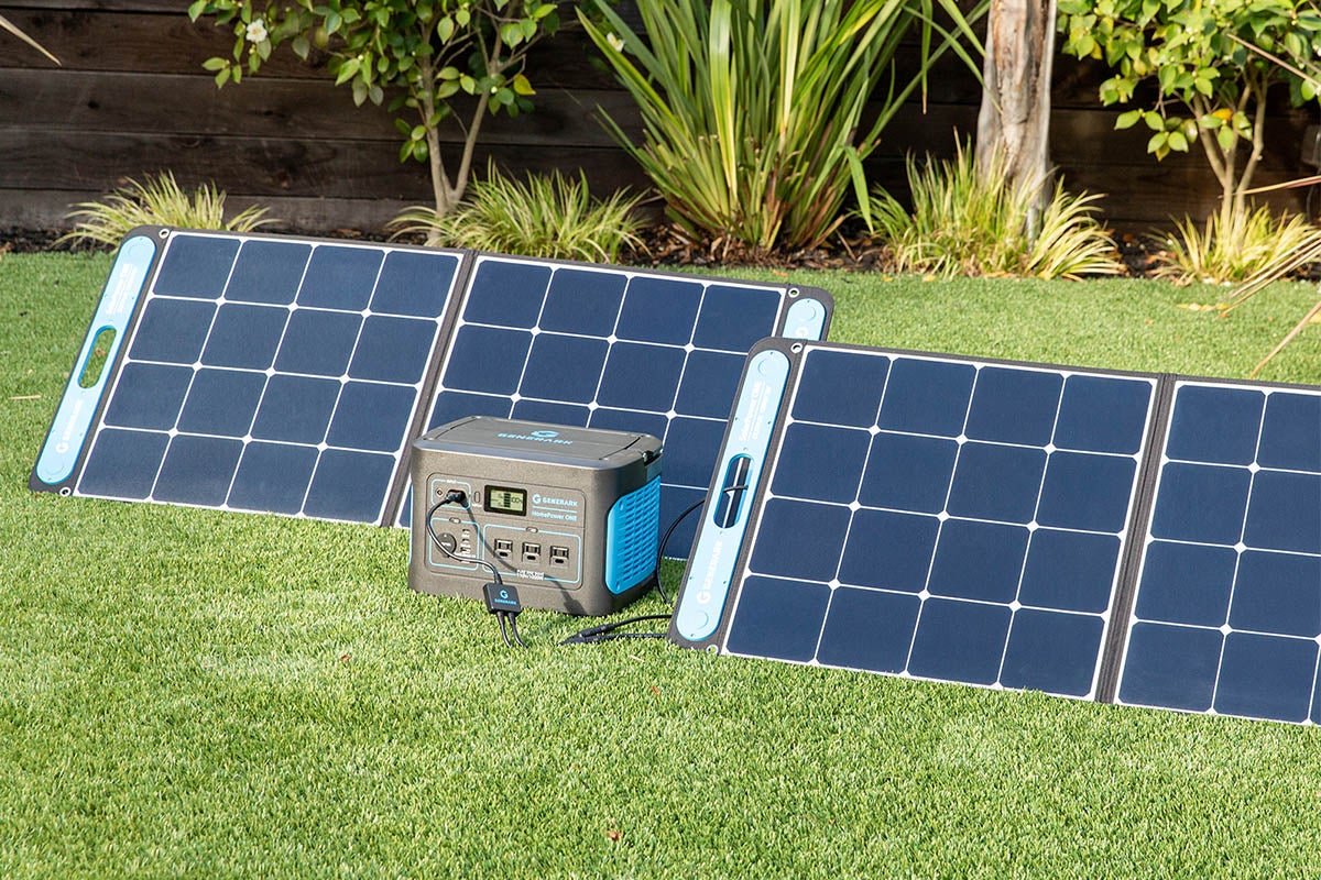 A solar generator sits on some grass flanked by solar panels.