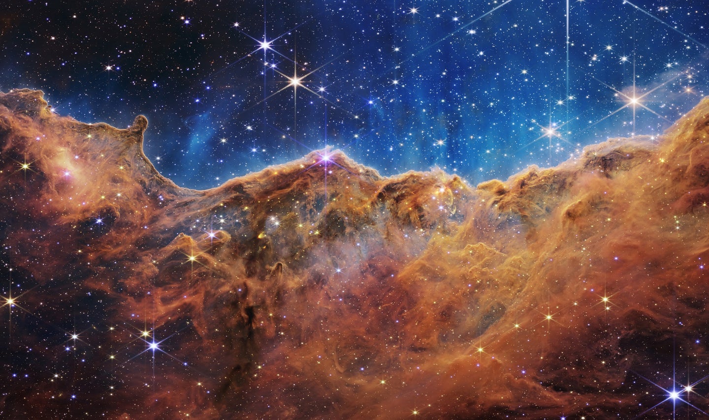 Starry valley of Carina Nebula against dust and light on a bluish universe in a James Webb Space Telescope image