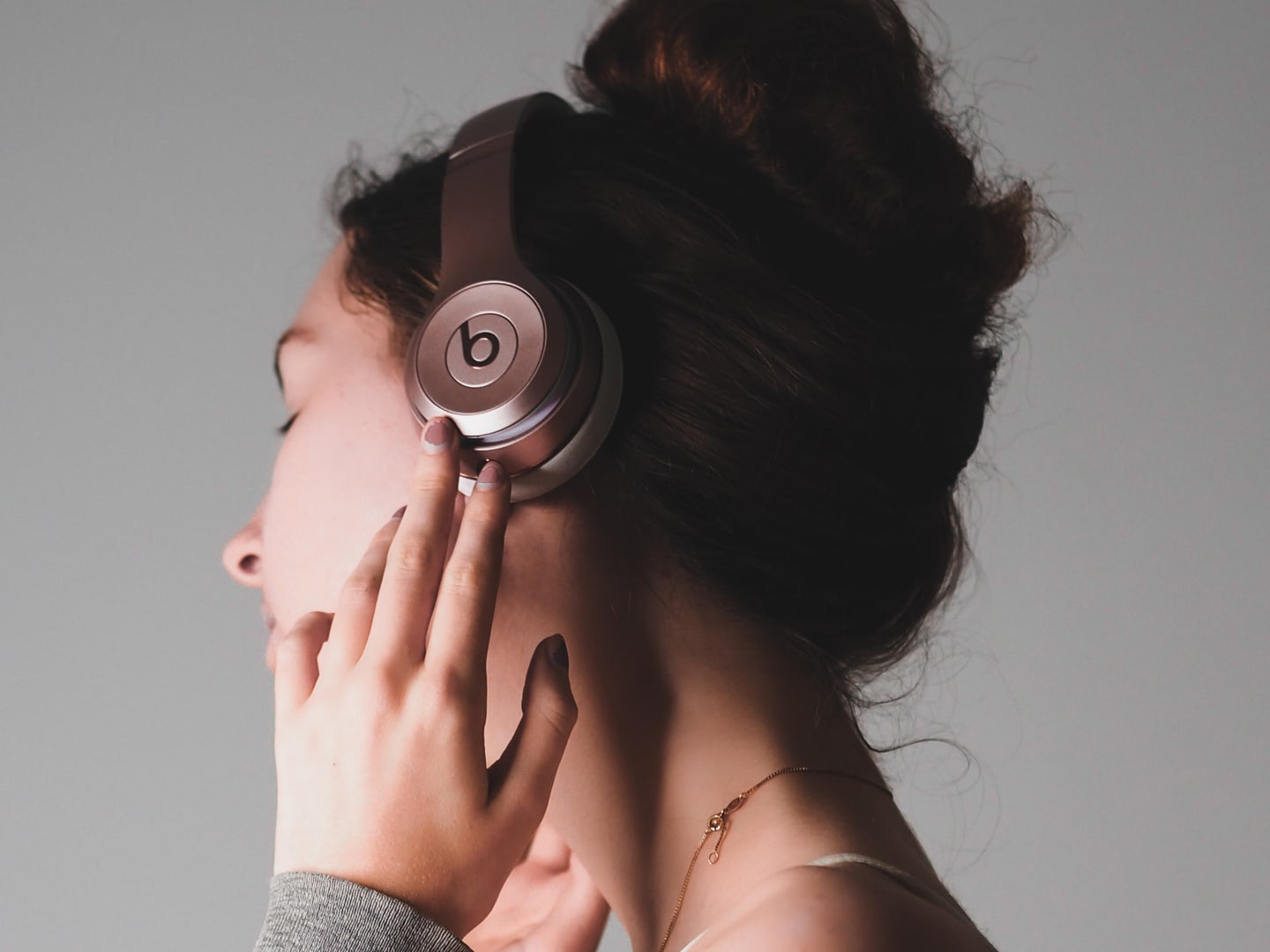 A brunette woman wearing pink headphones and looking away from the camera as she listens to music she owns that she put onto her Spotify playlist.