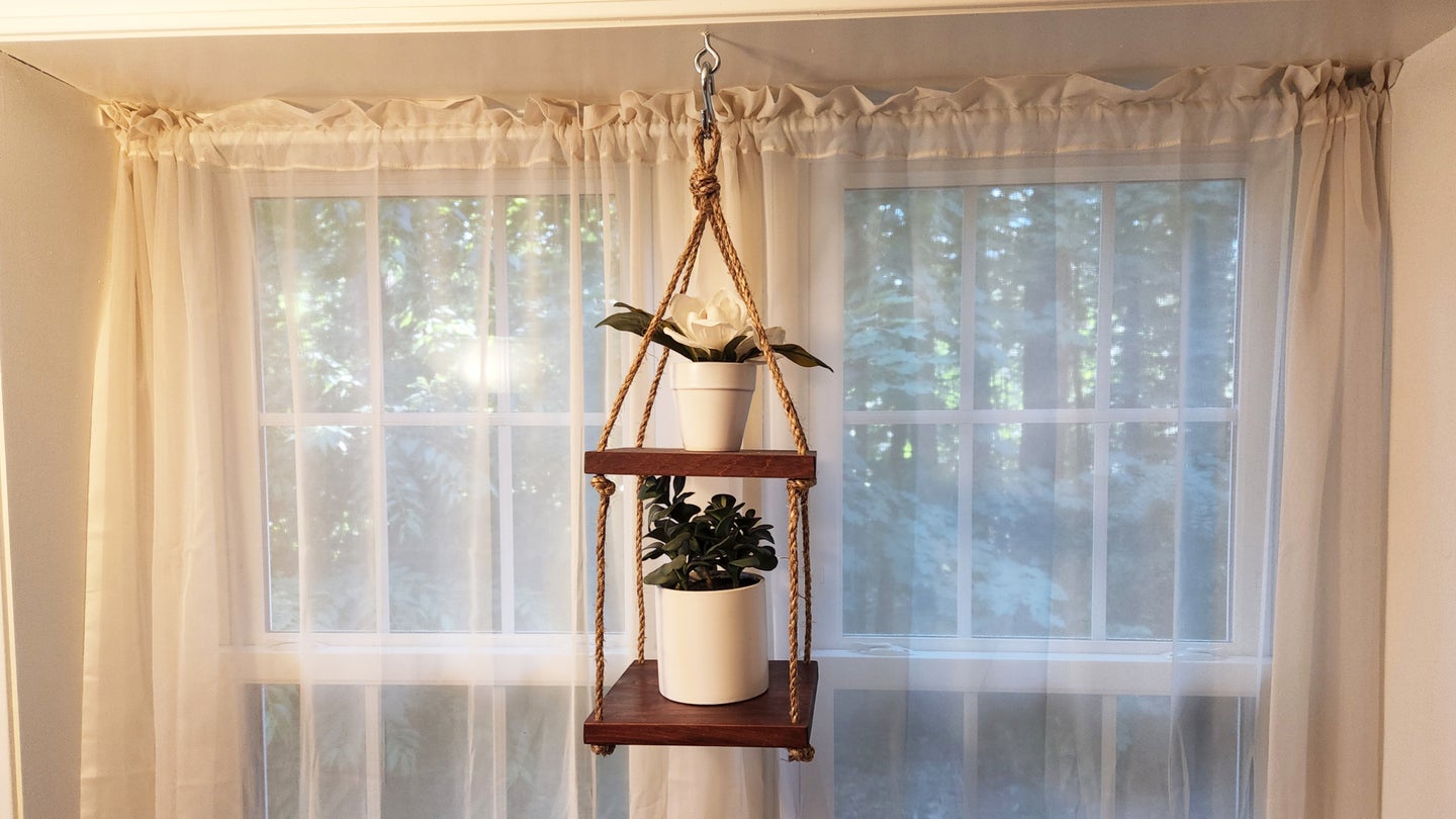 A DIY plant hanger made out of two pieces of wood and some rope.