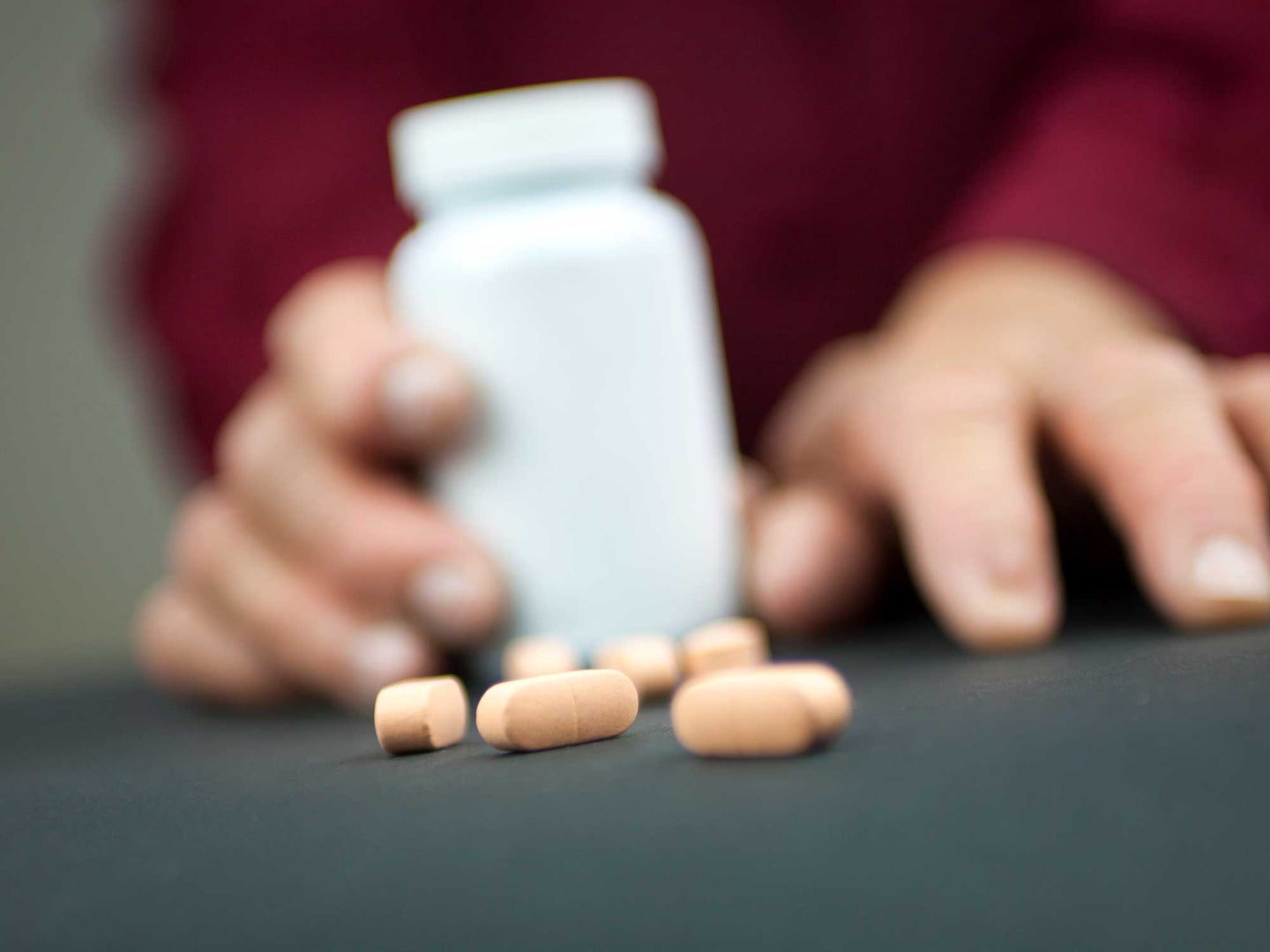 Hands holding a box of pills, pills in the foreground and the background is out of focus.