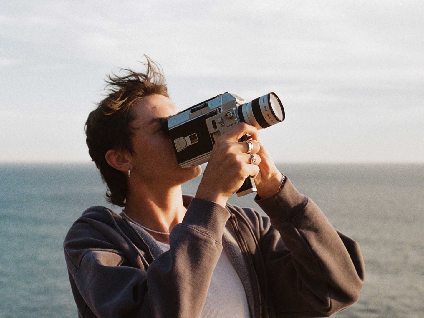 A person shooting with a Super 8 camera on the beach pointing at the sky.