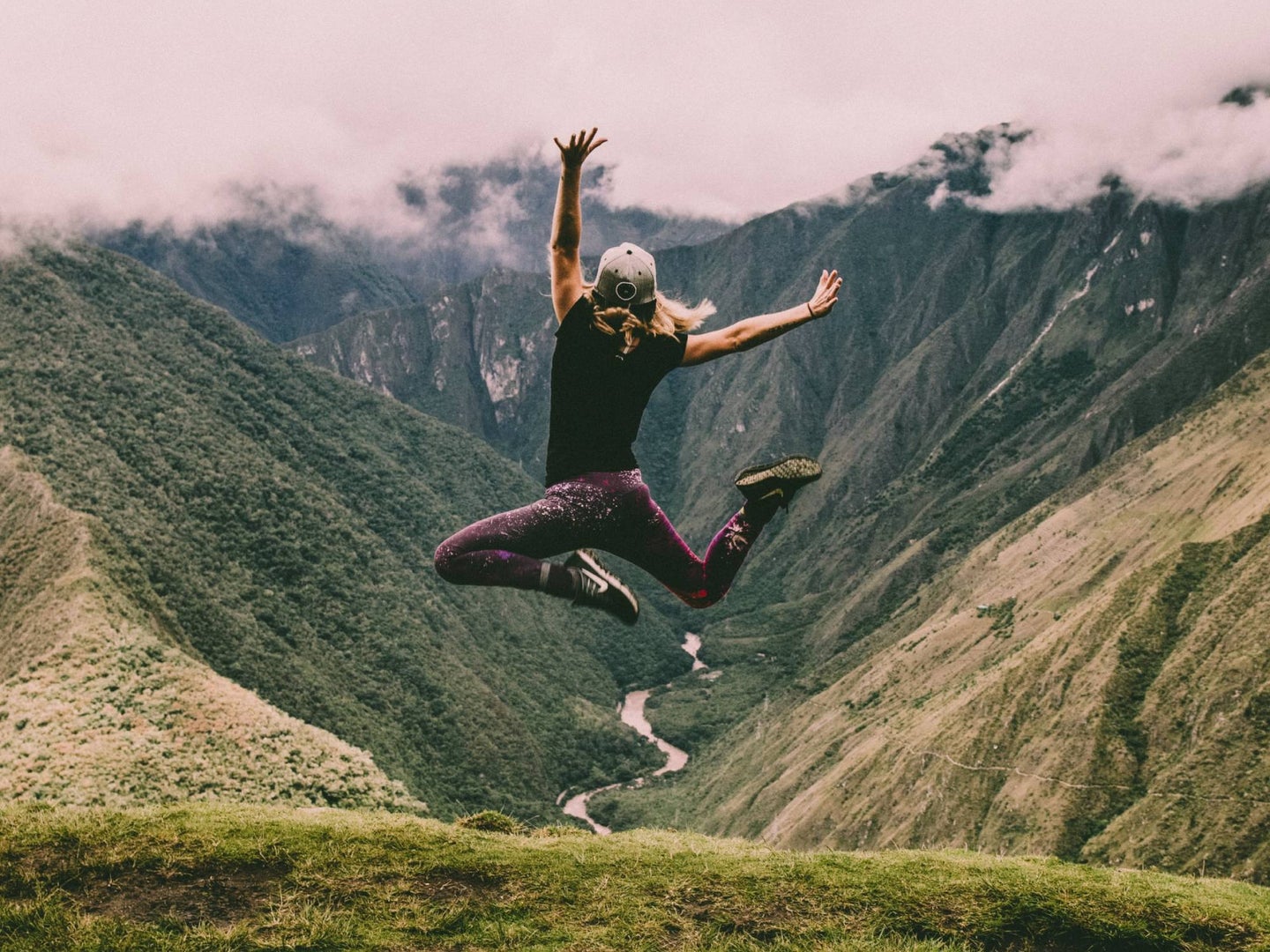 Person jumping on a hill with mountains on the background