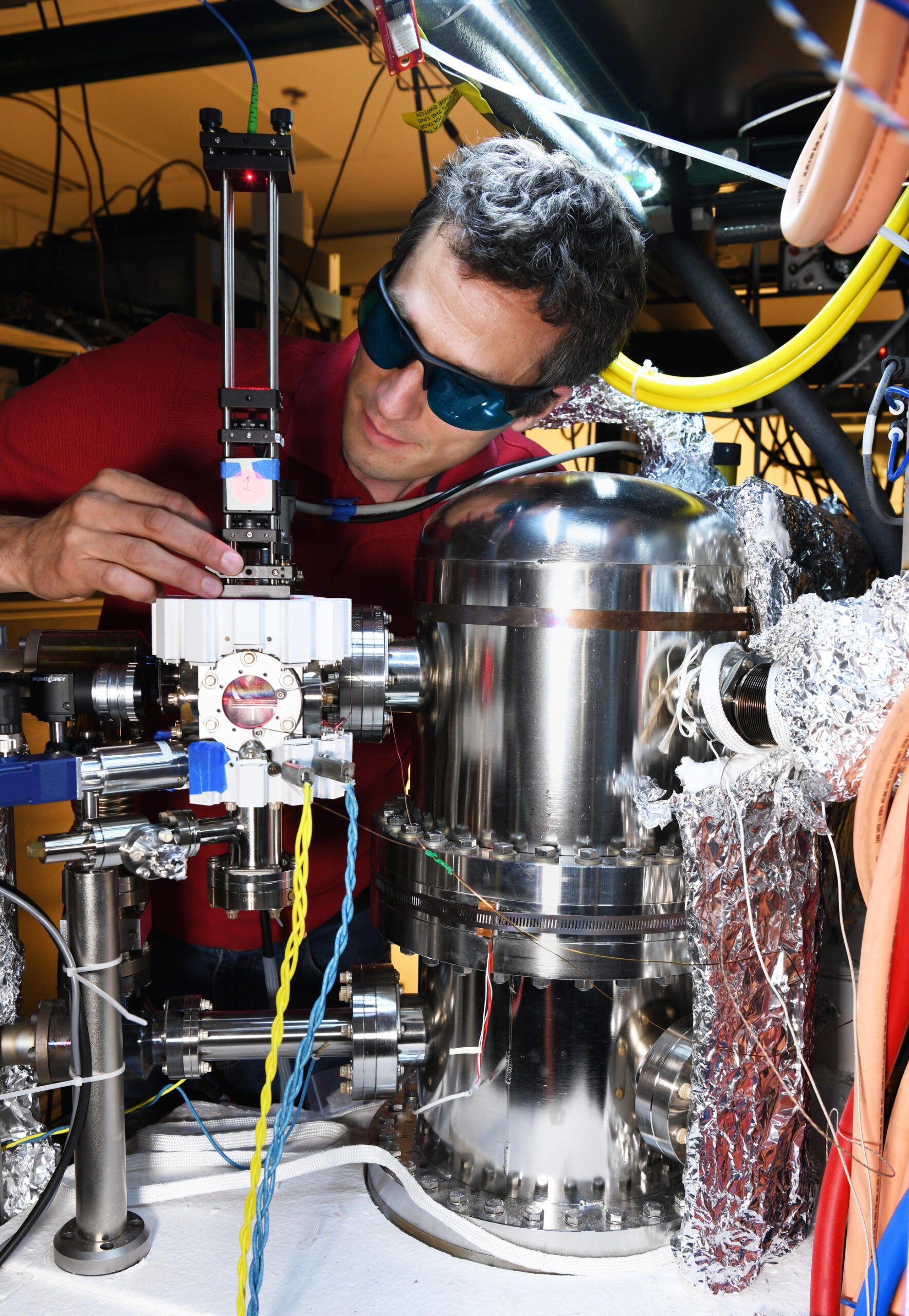 NIST engineer in red polo and glasses testing silver cold-atom vacuum chamber