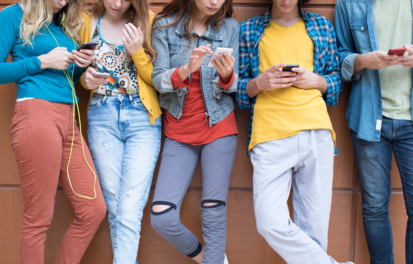 Four teens standing in a row using their smartphones