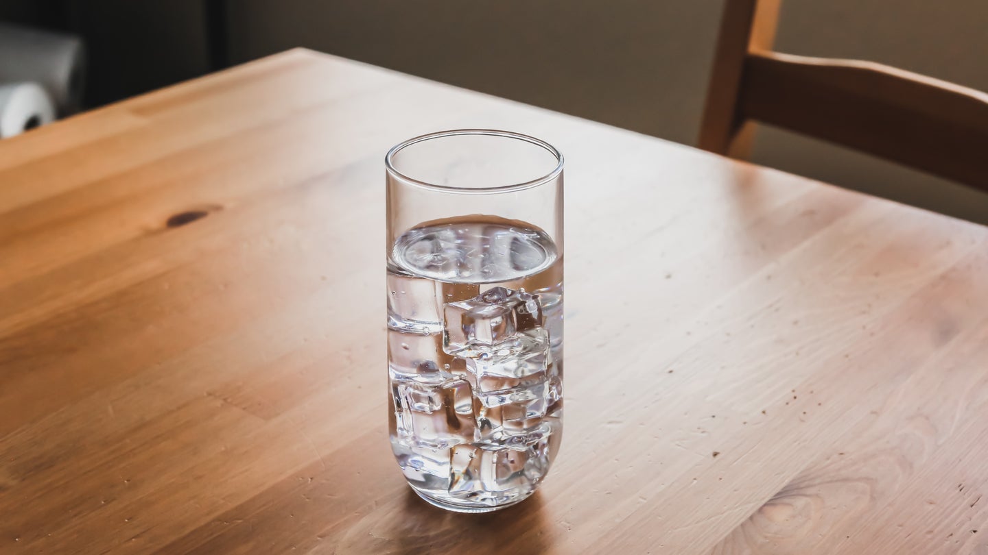 A glass of water with crystal-clear ice cubes in it on a sunlit wooden table.