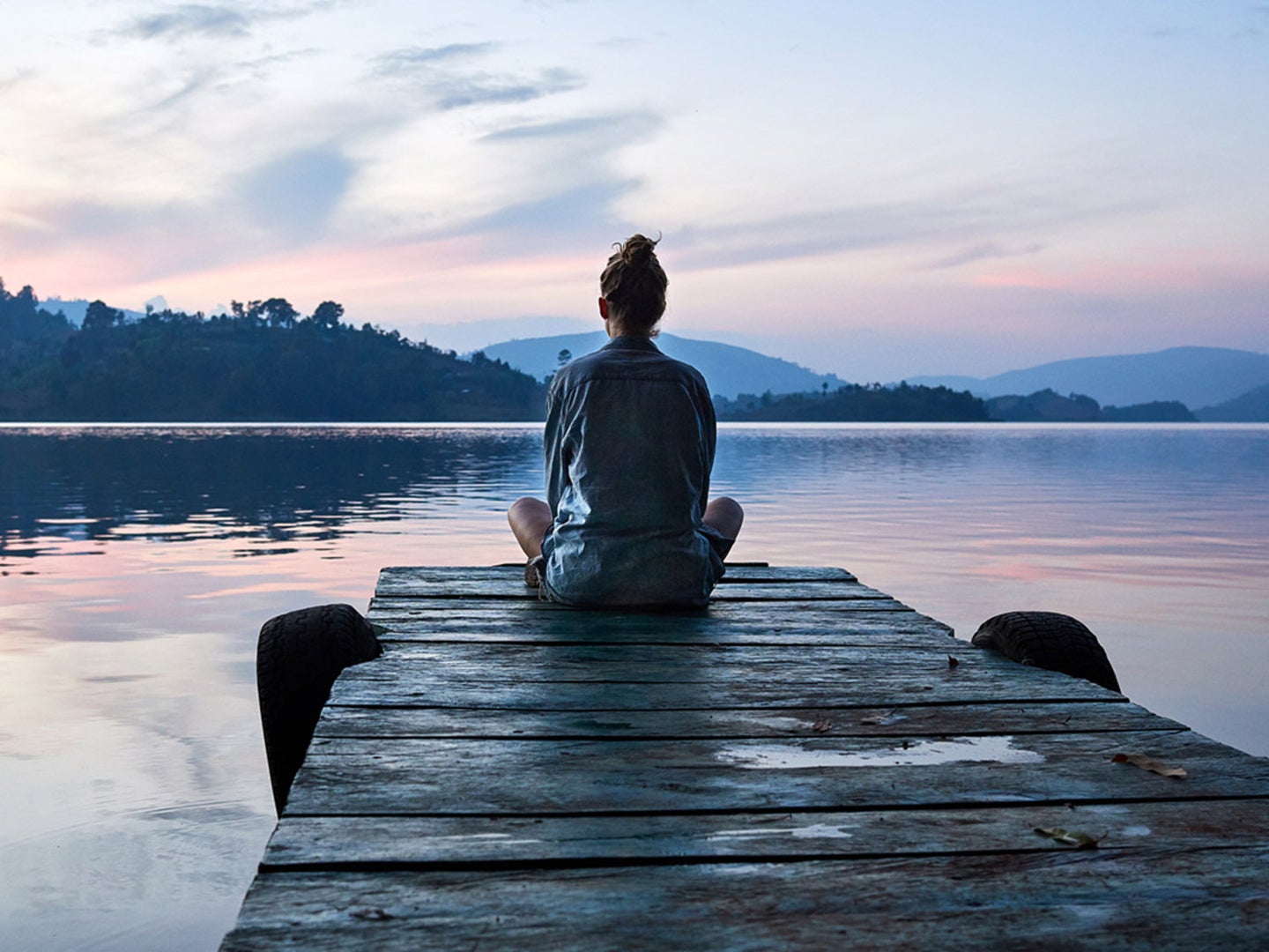 A person practicing mindfulness by meditating on a dock by a lake