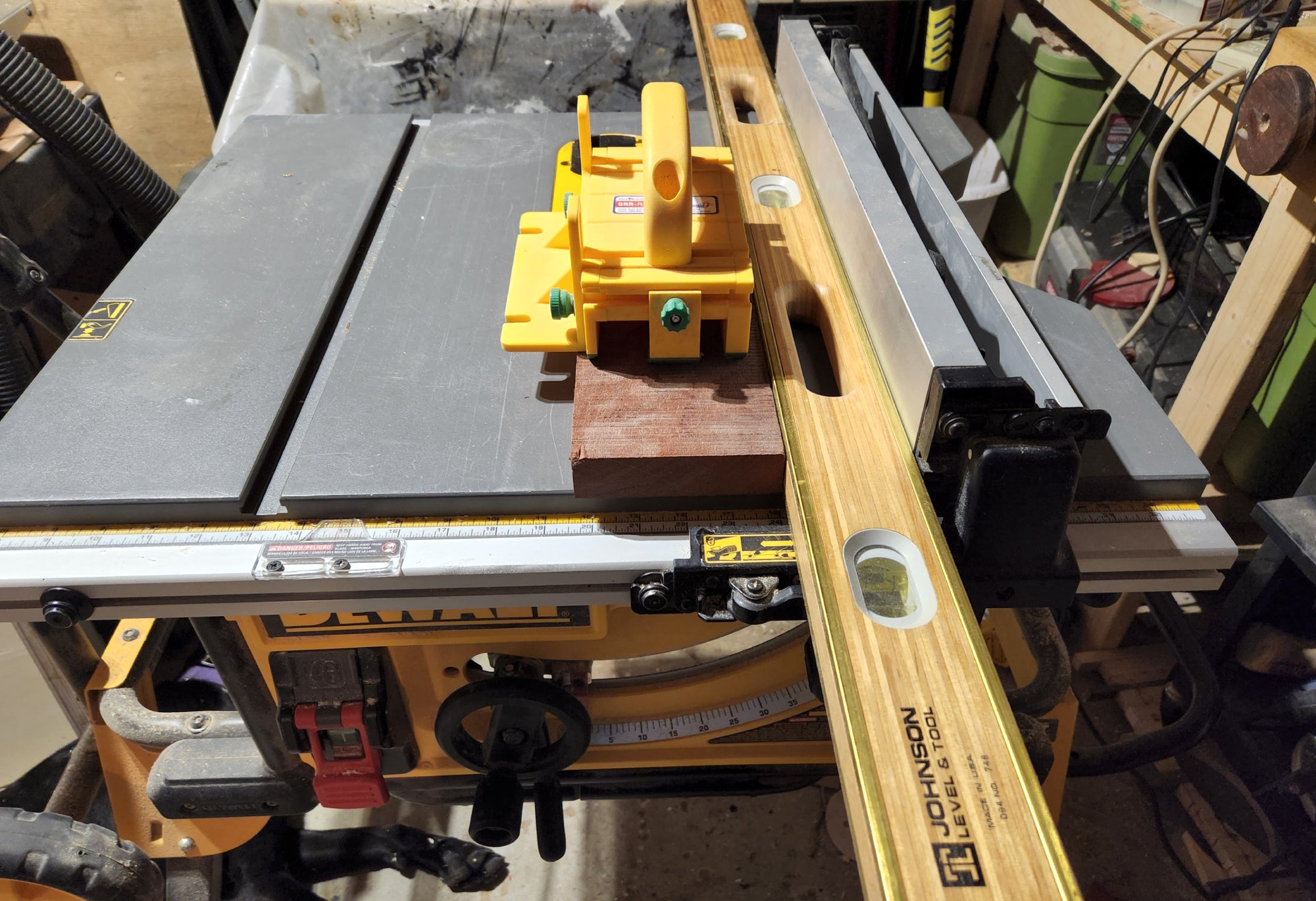 A person using a level to joint wood without a jointer, by having the level pressed against their table saw fence as a guide for the piece of wood. They're also using a push block for safety.