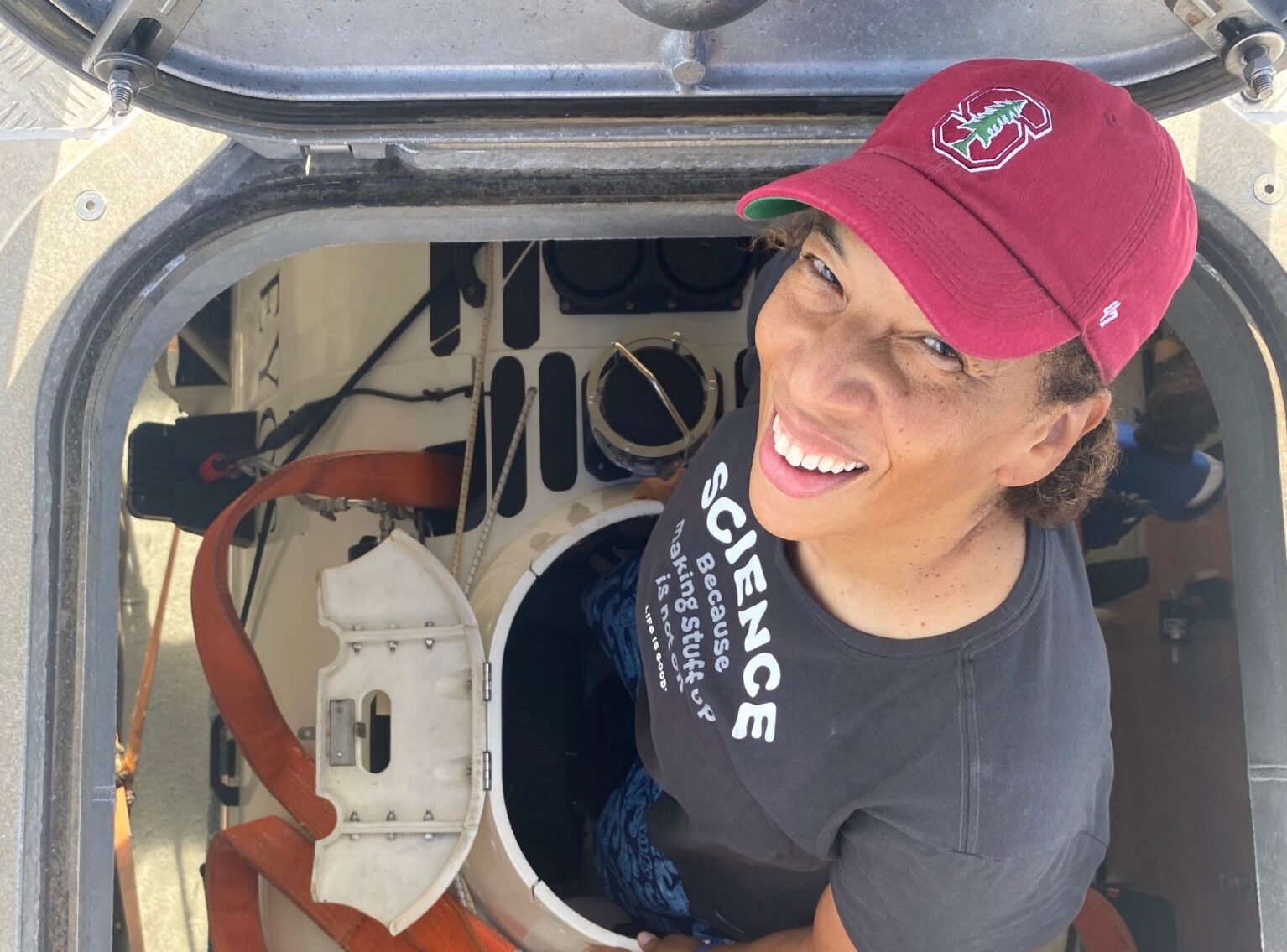 a black woman in a stanford baseball cap stands in the hatch of a submersible about to load