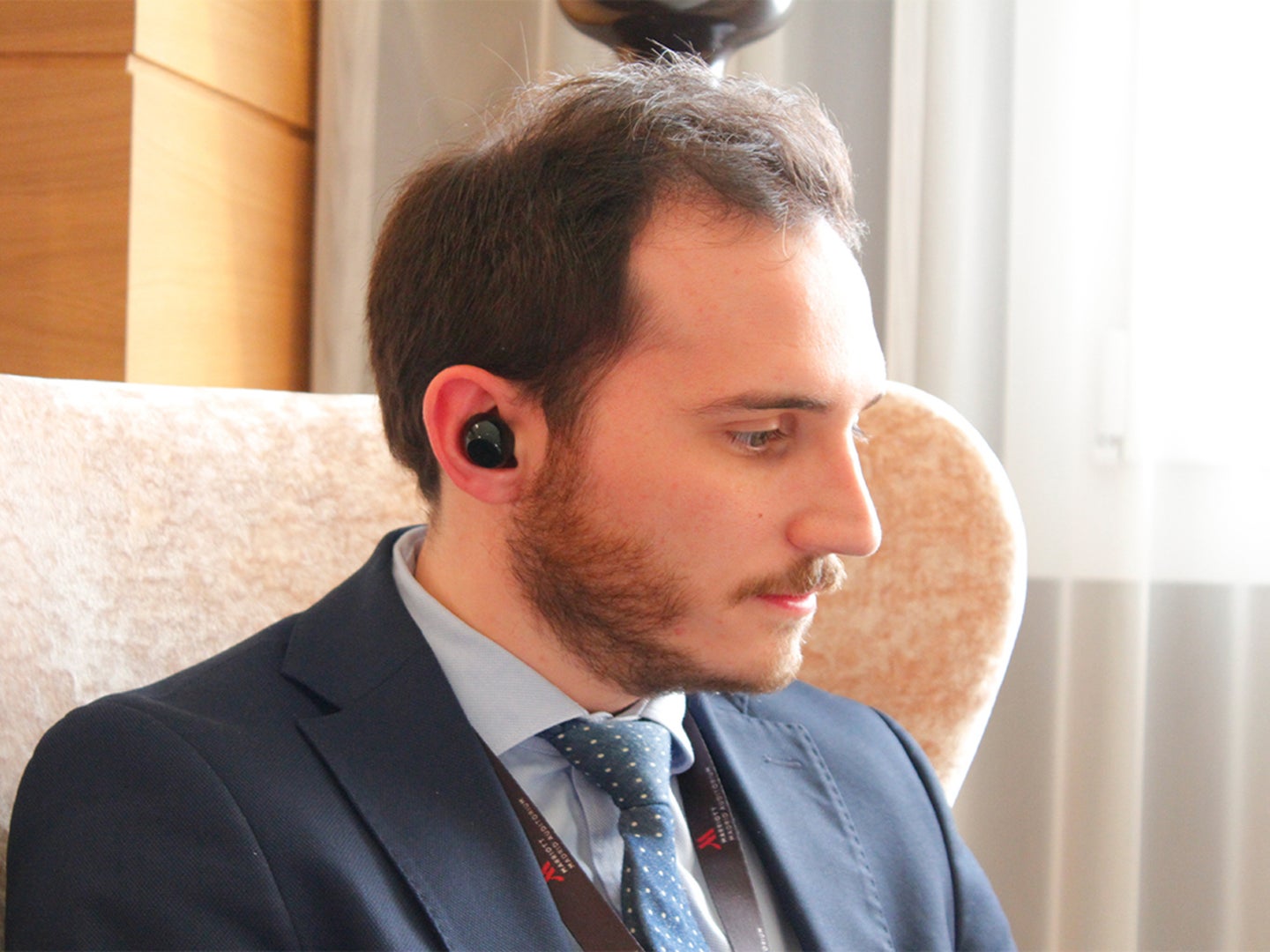 A man wearing a suit wearing wireless headphones and staring off to the side