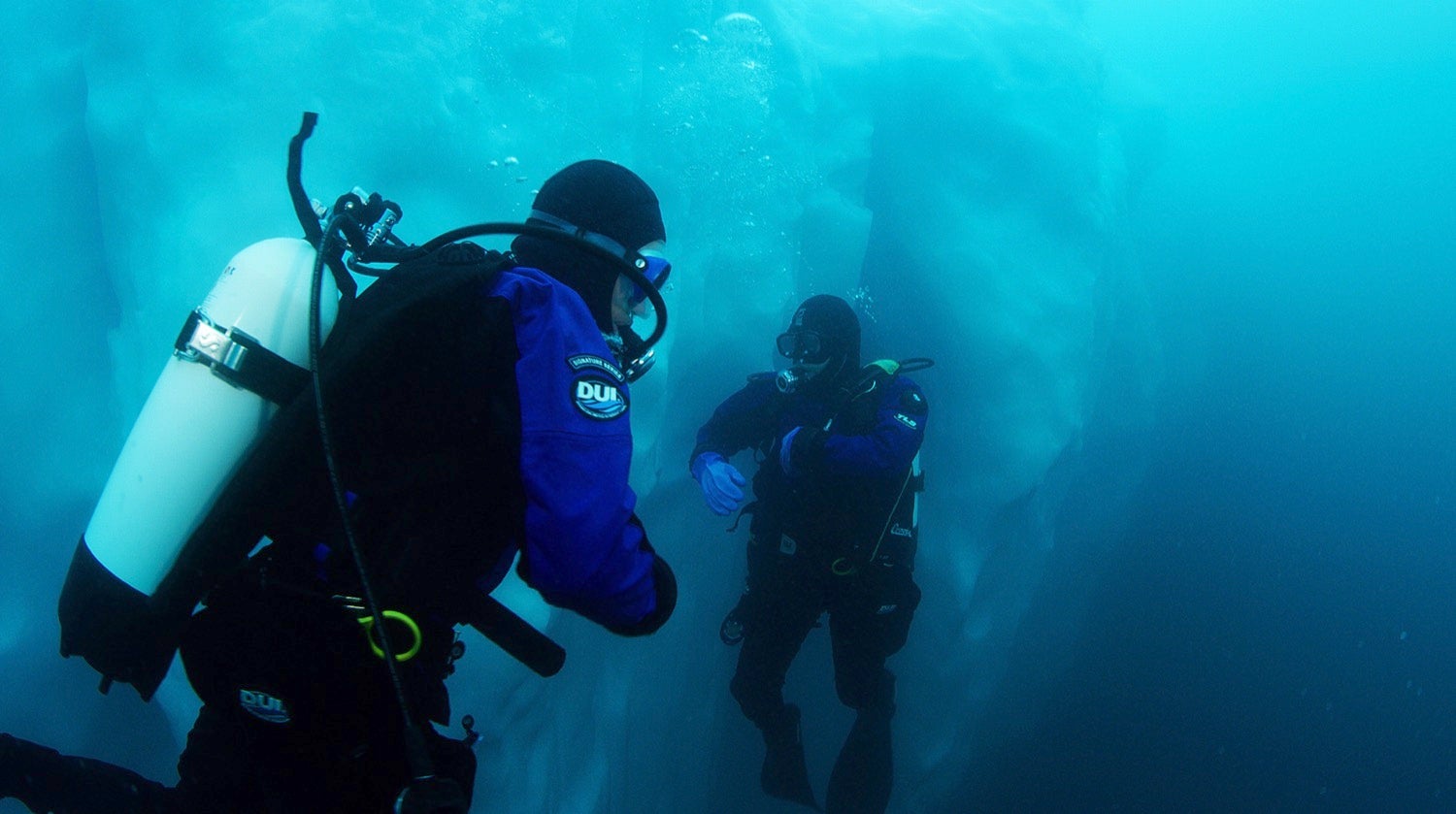 two people in scuba gear under the water near an iceburg