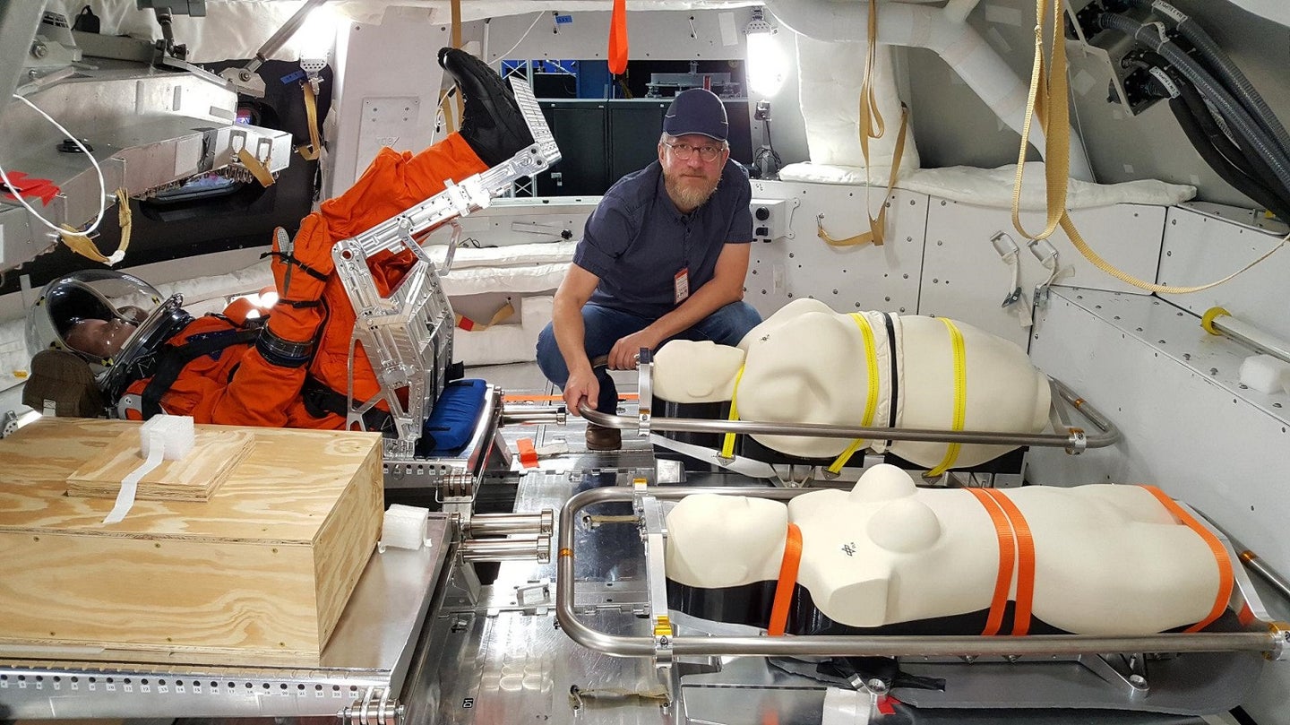 NASA collaborator crouching in Orion capsule with three strapped-in mannequins for Artemis I mission