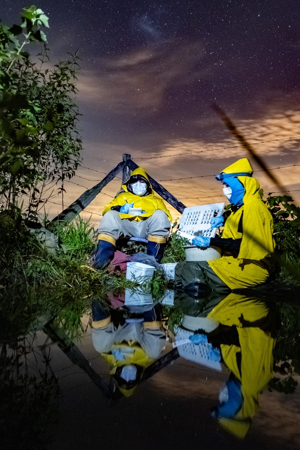 Forscher in gelben Schutzanzügen und COVID-PSA nachts unter einem Sternenhimmel