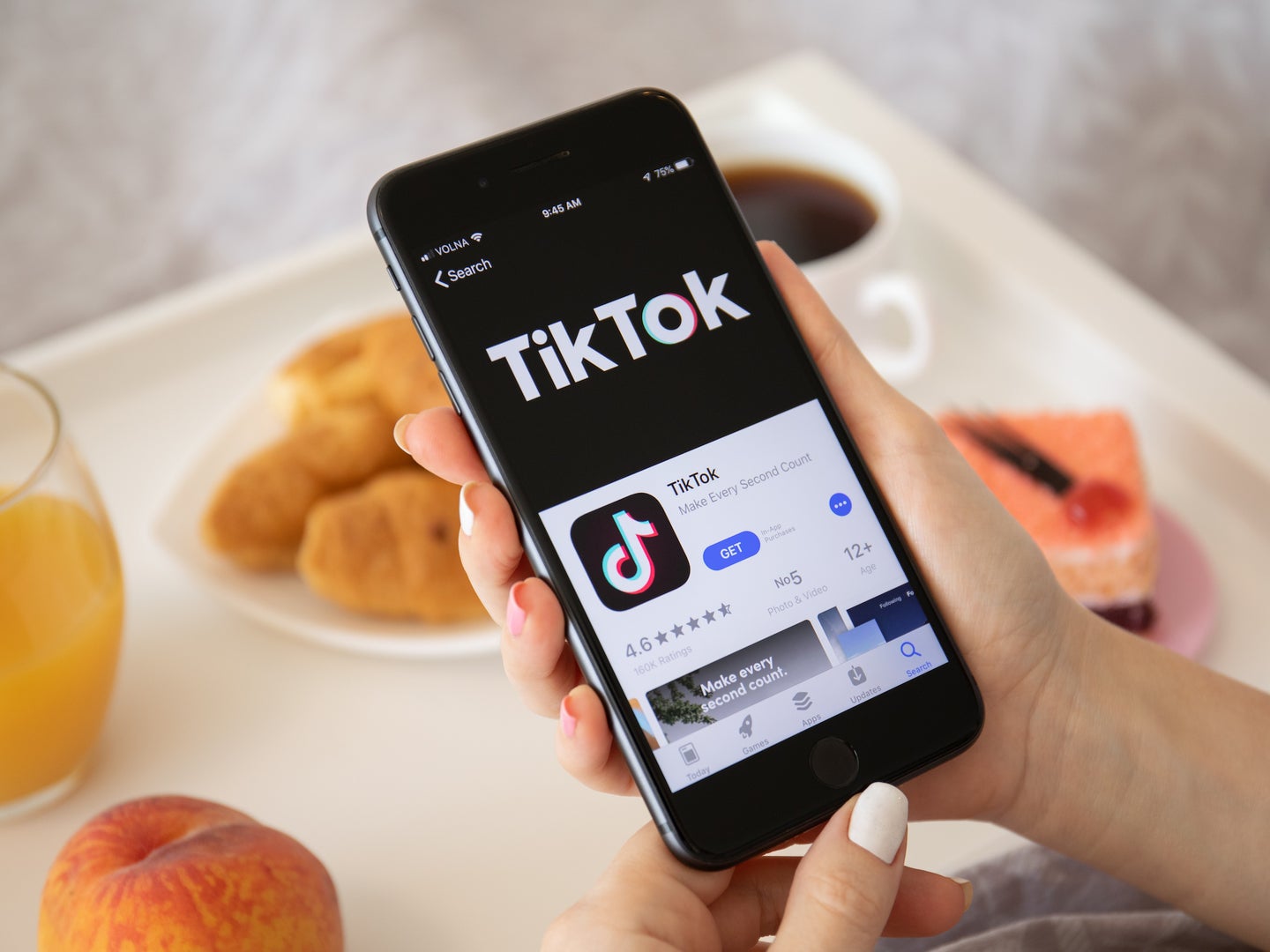 Woman holding smartphone displaying TikTok download page above table