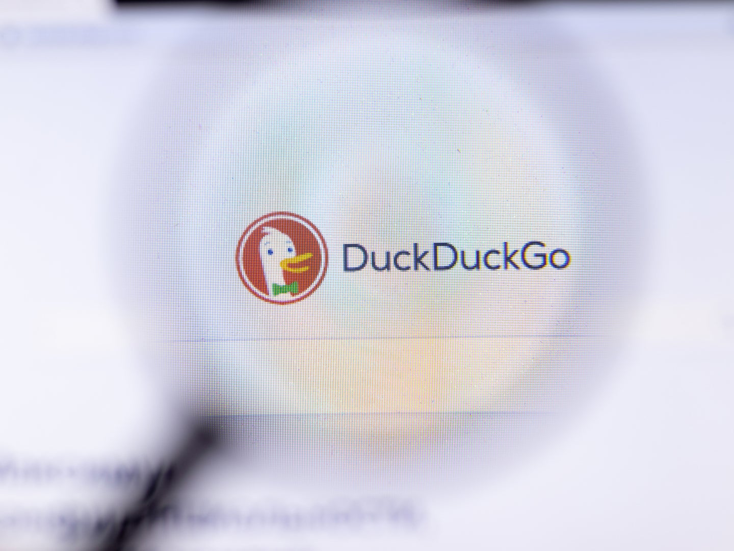 Out of focus magnifying glass lens hovering over DuckDuckGo search engine homepage