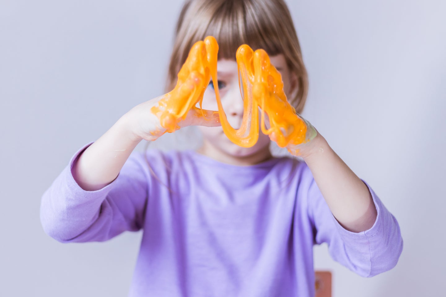 Kid in lavender shirt stretching toy orange slime out with hands