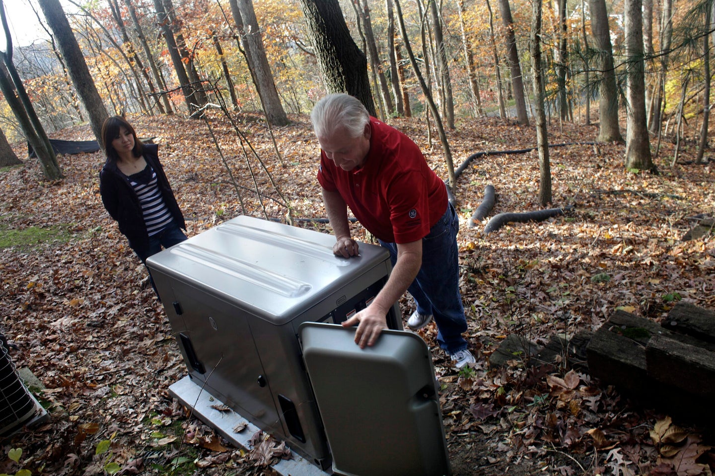 Two elderly people looking at a large grey generator in the woods