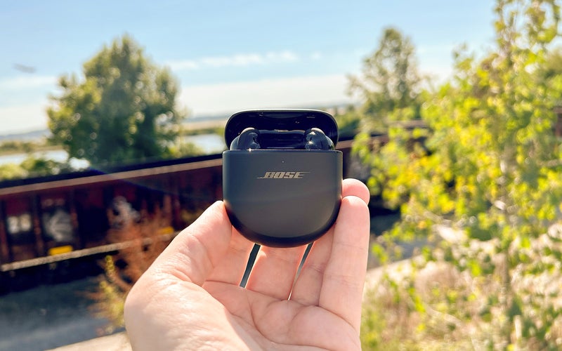 Bose QuietComfort Earbuds II outside with a train and plane in the background