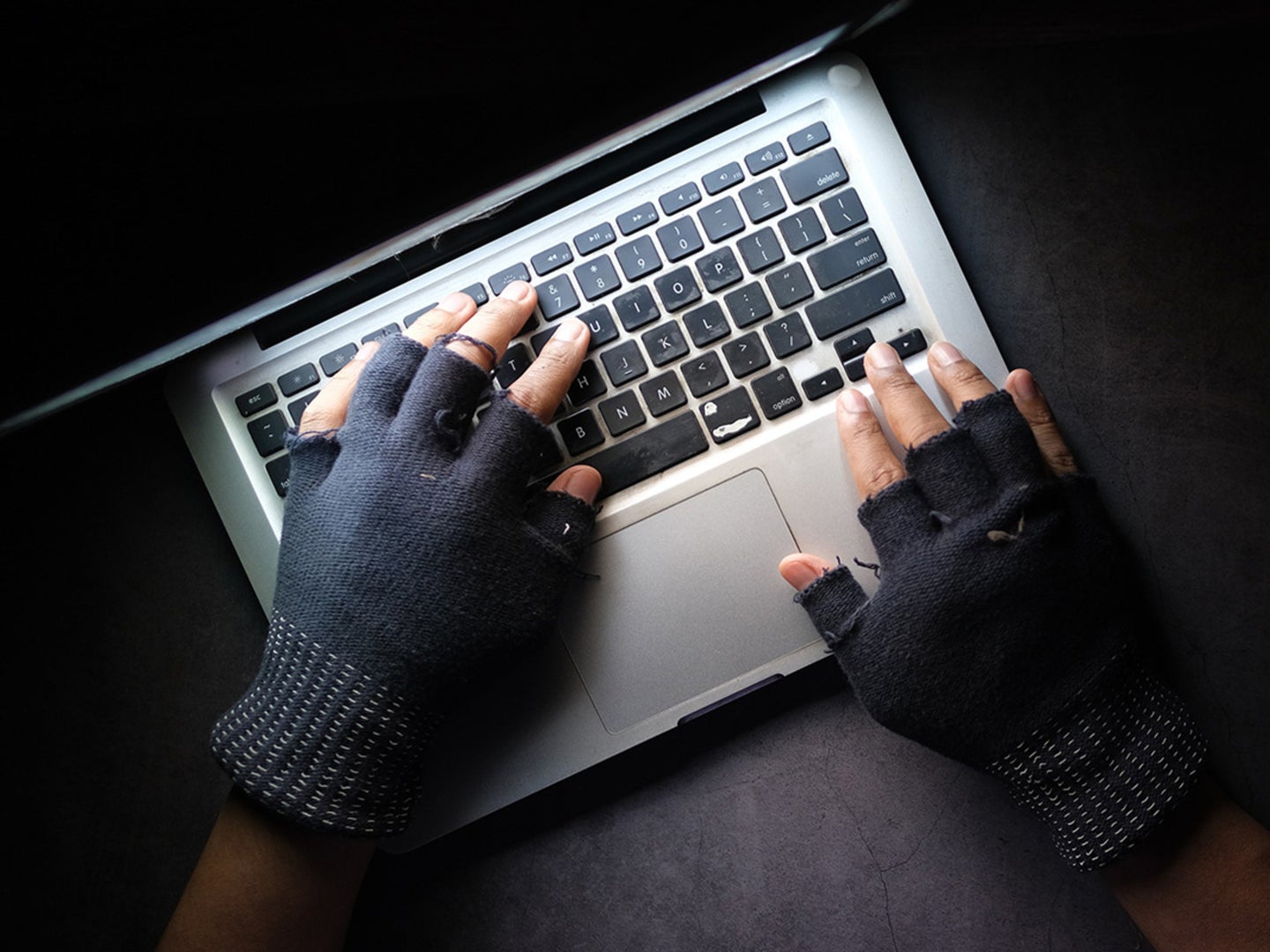 A hacker wearing gloves coding on a laptop