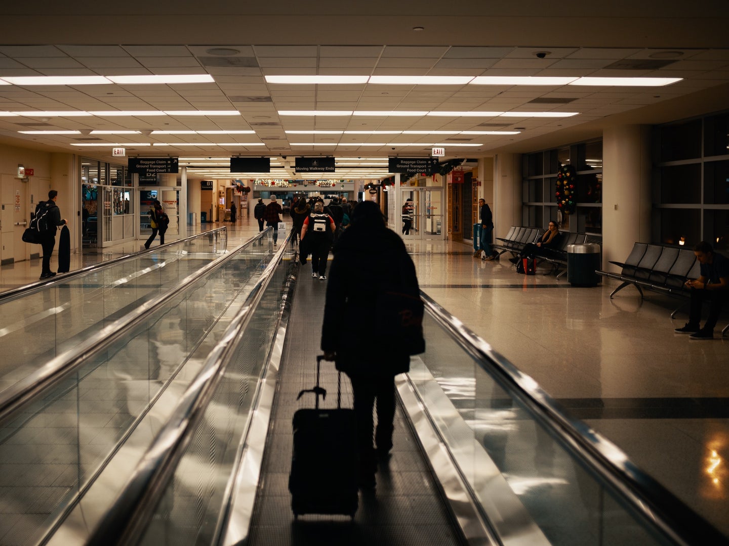 Traveller walking down conveyor belt walkway with luggage in airport