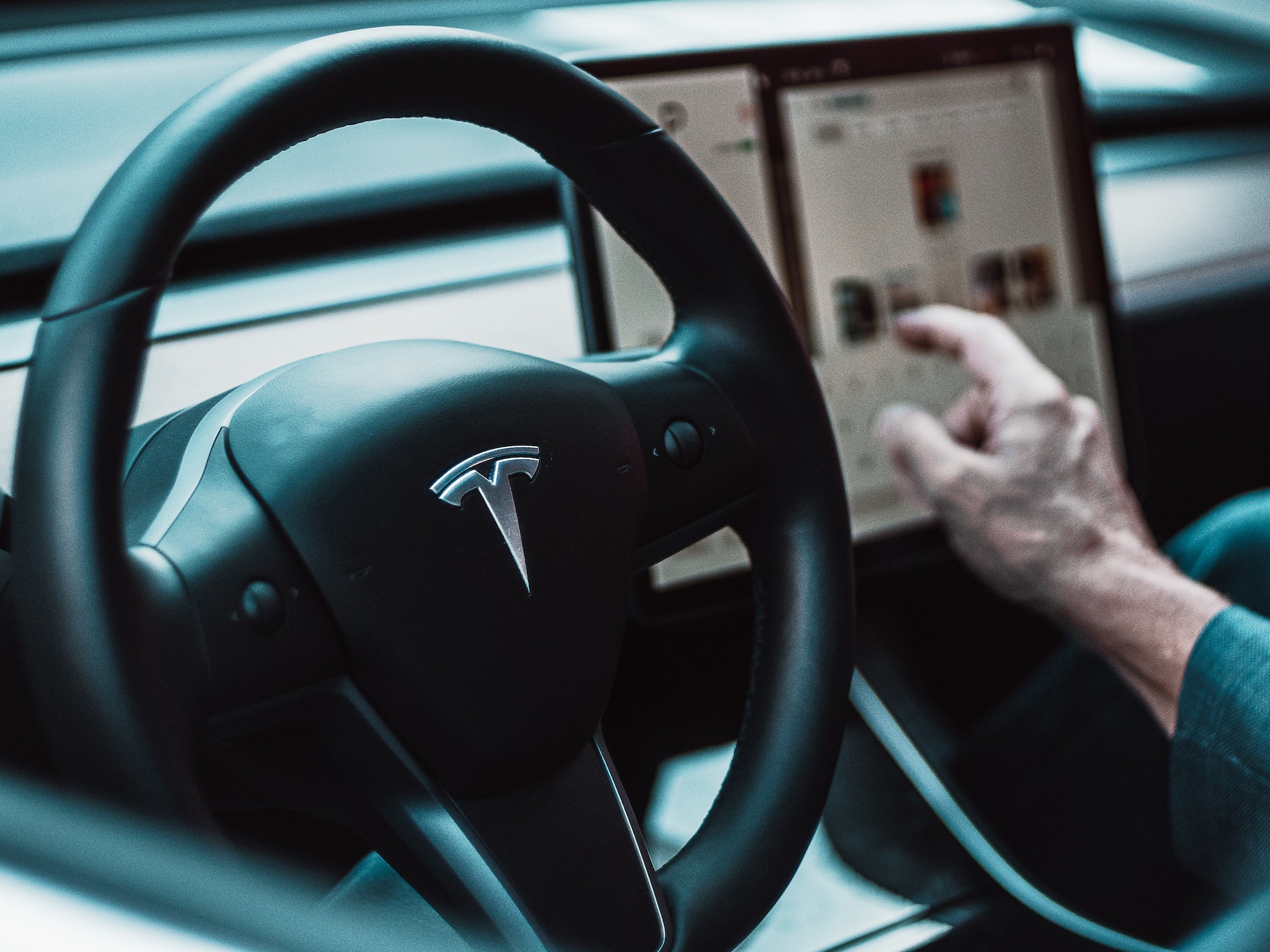 Tesla interior with driver hand on black steering wheel