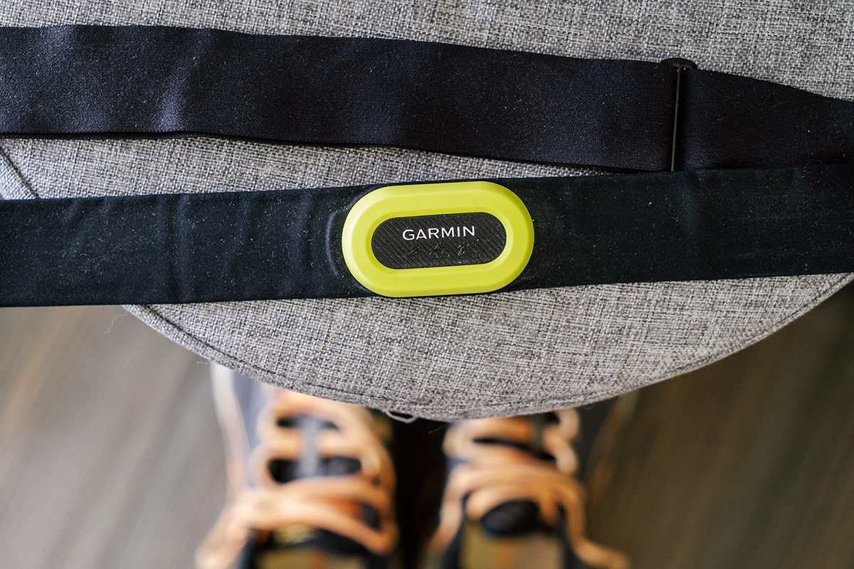 A black and yellow Garmin HRM Pro Chest Heart Rate Monitor sitting on an ottoman above a pair of hiking boots.