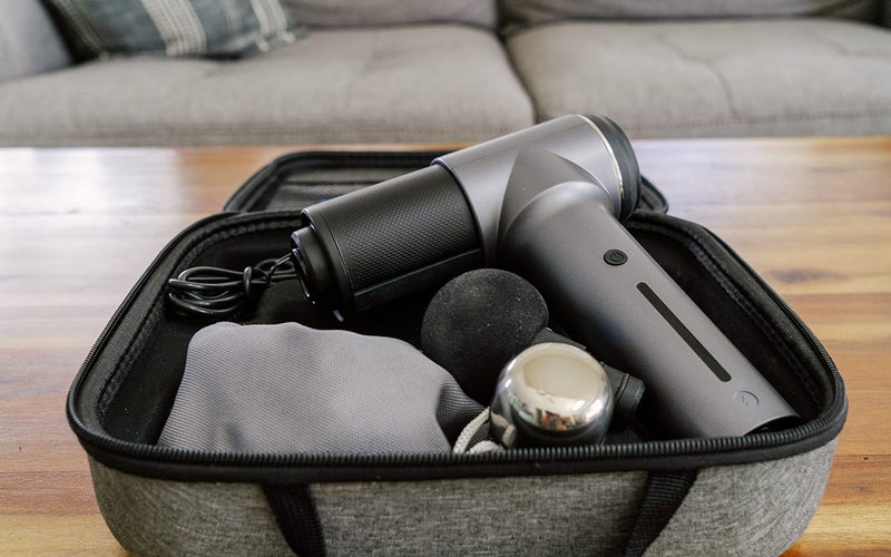 A gray and black Turonic GM5 Massage Gun with accessories in a gray fabric case.