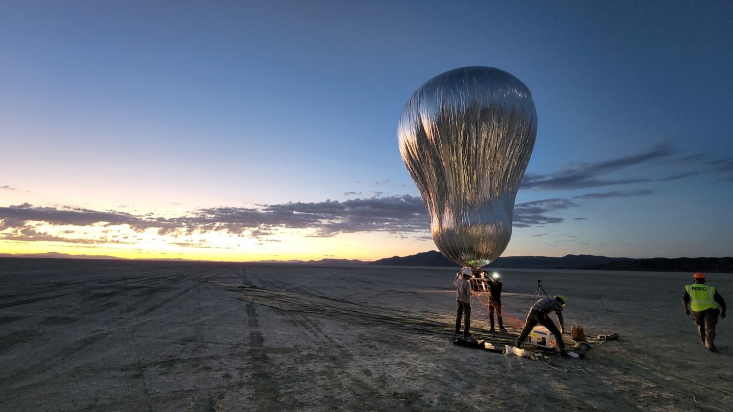 a silver balloon is inflating in a desert as the sun rises