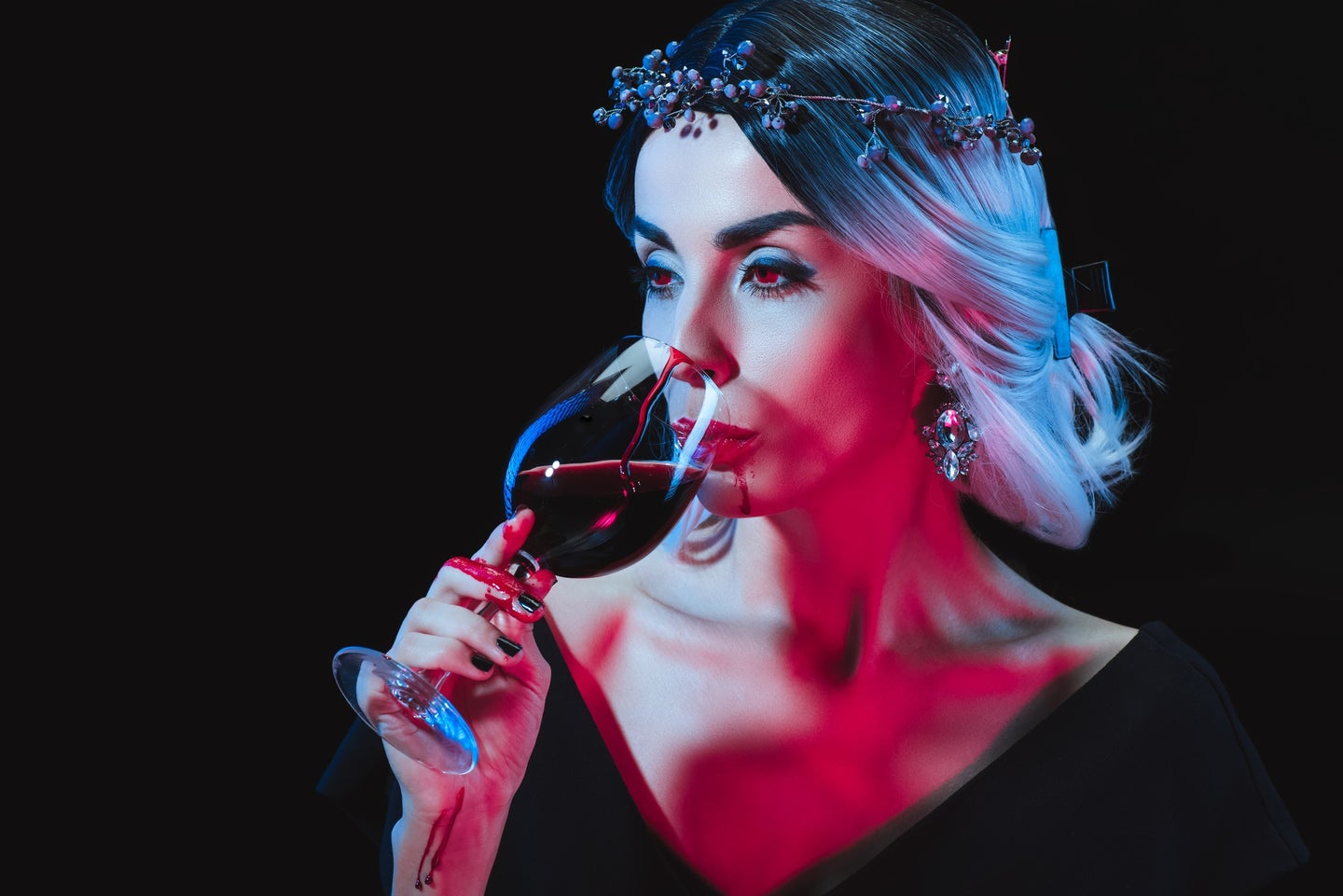 Pale-skinned person with silver hair in black dress to look like vampire sipping on a glass of red wine or blood