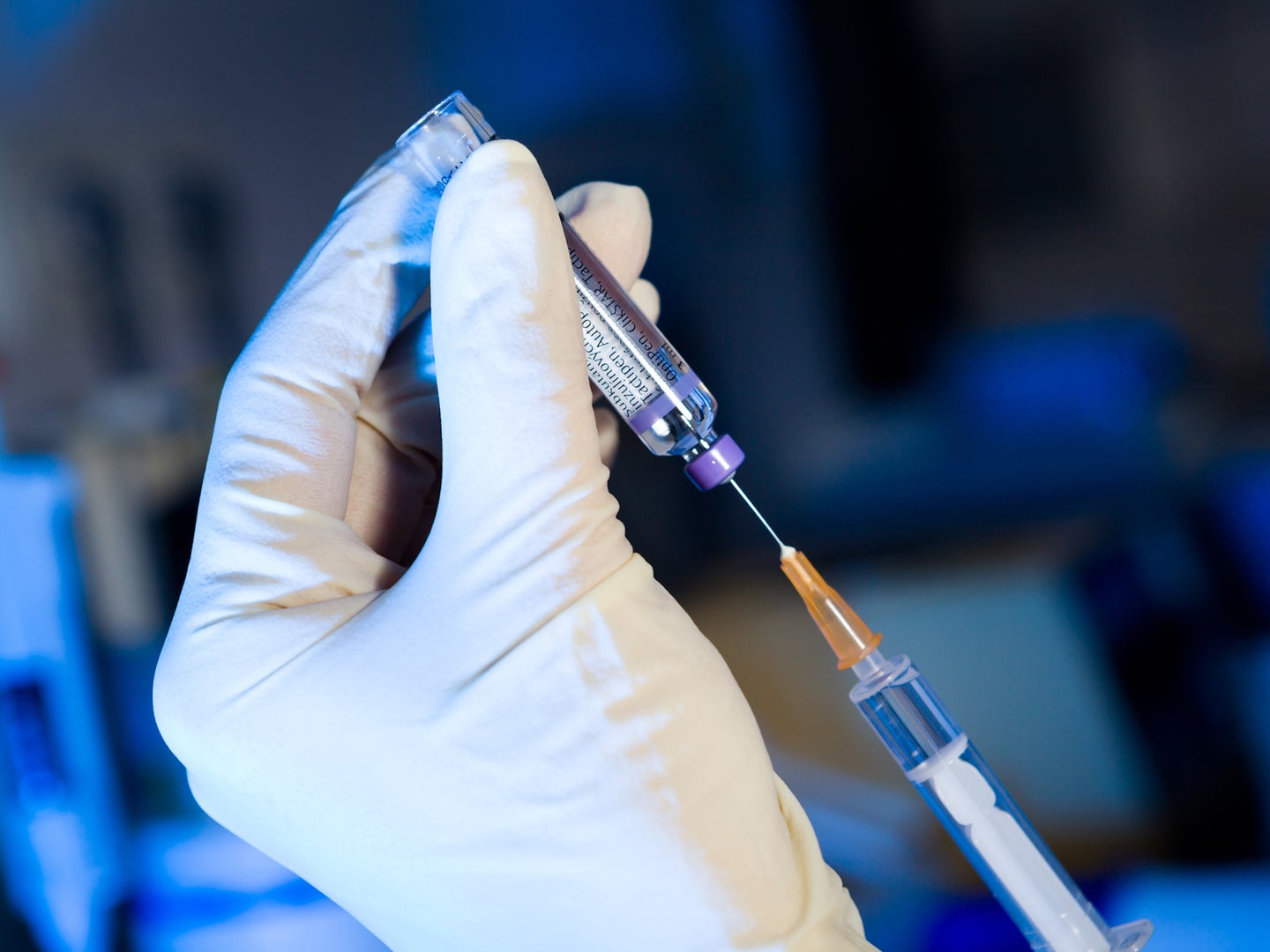Scientist's gloved hands using syringe to fill vaccine shot