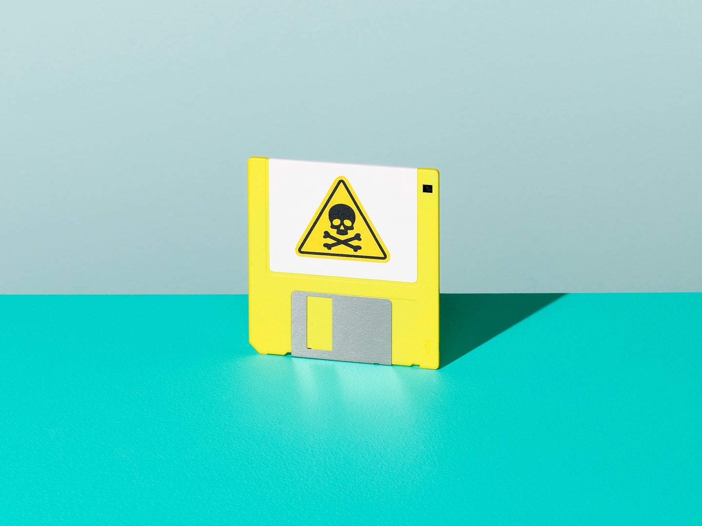 A yellow floppy disk with a poison symbol on it, standing upright on a teal surface.