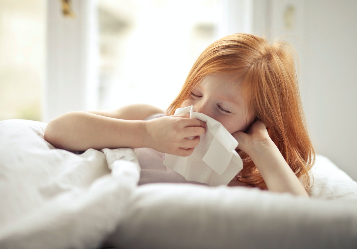 A young girl in bed wipes her nose.