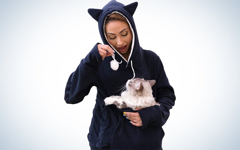A woman wearing a navy blue cat hoodie with a cat in the pouch.