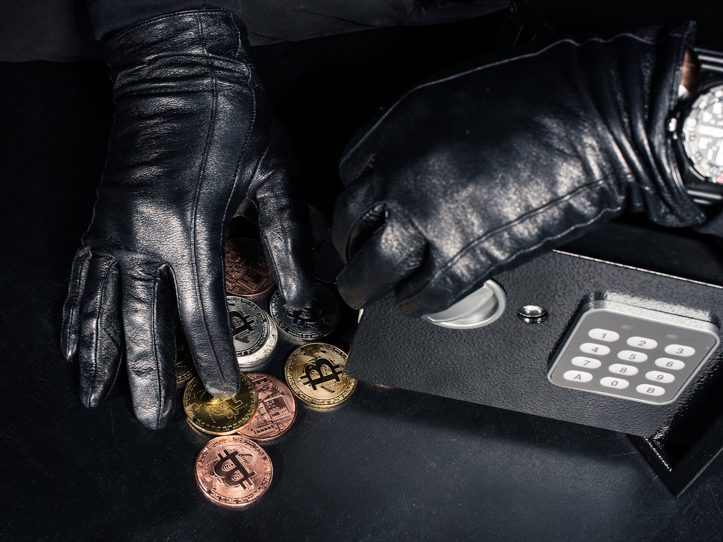 Black gloved hands stealing physical Bitcoins from small safe